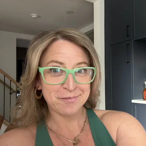 Portrait of Dani Eve wearing mint green glasses and a green top, with a calm half smile.
